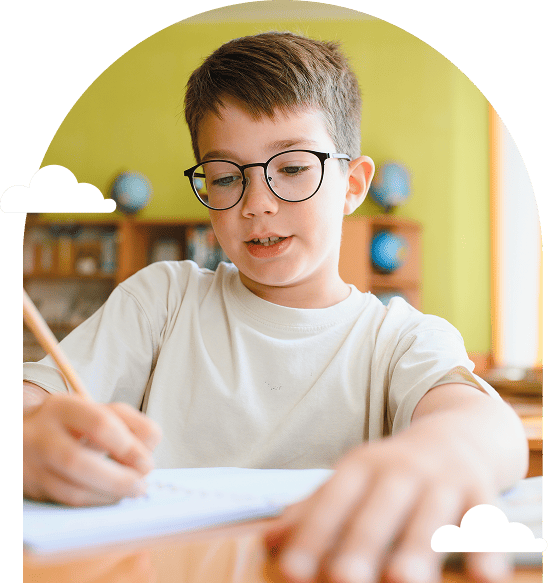 young boy with glasses writing at a desk in a classroom